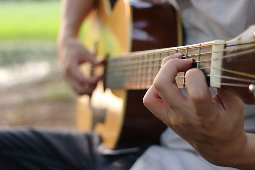 Selective focus of finger of guitarist playing acoustic guitar on blurred nature background.